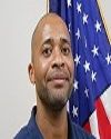 African American male in blue shirt poses in front of American flag