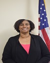 African American female in pink shirt with black blazer poses in front of American flag